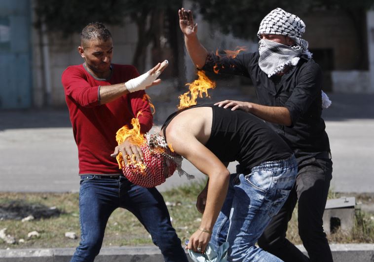 Palestinian protesters put out a fire burning on a compatriot, caused by a Molotov cocktail 