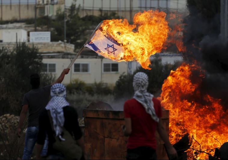 A Palestinian demonstrator sets fire to an Israeli flag near the West Bank settlement of Beit El
