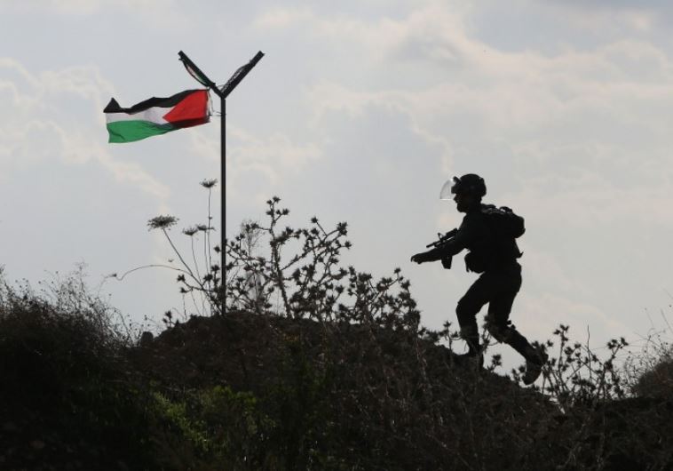 A member of the Israeli security forces runs past a Palestinian flag during clashes