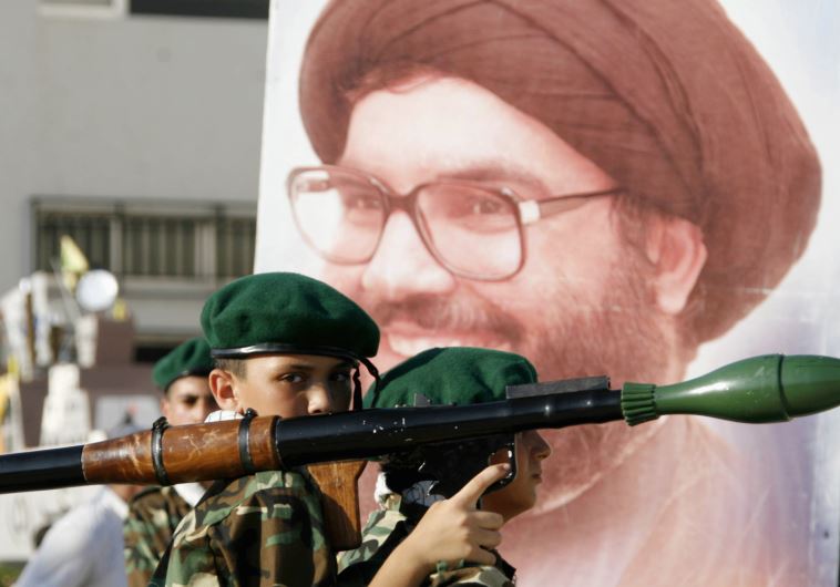 A Hezbollah member carries a mock rocket next to a poster of the group's leader, Hassan Nasrallah