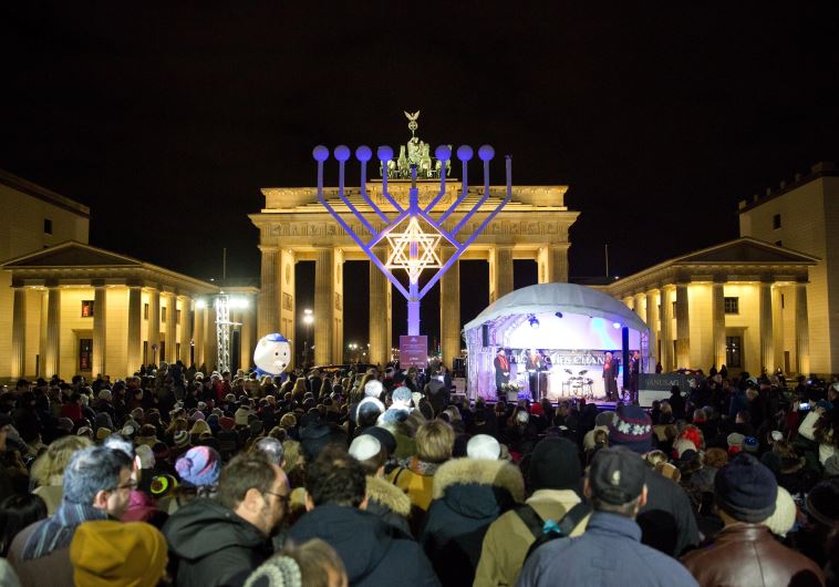 People stand in front of a giant eight- branched candelabrum Menorah in front of the Brandenburg Gat