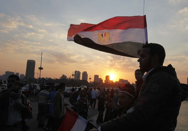 People stand on a bridge overlooking the river Nile as many Egyptians walk on the streets 