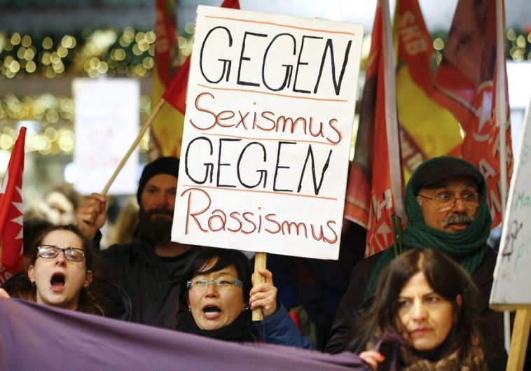 Women shout slogans and hold up a placard that reads "Against Sexism - Against Racism" 