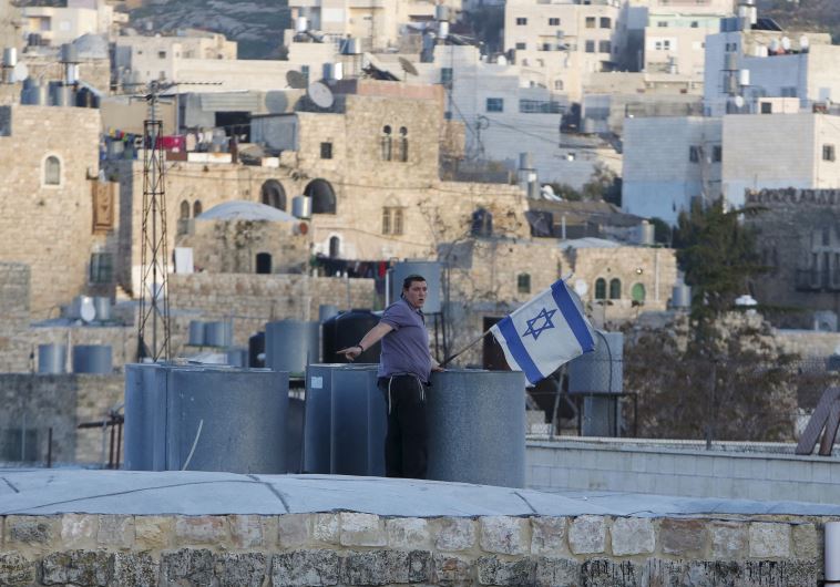 An Israeli settler puts up an Israeli flag over a house in Hebron