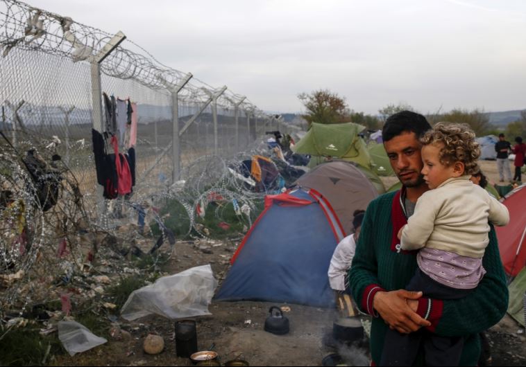 A man with a child looks at the border fence at a makeshift camp for migrants and refugees