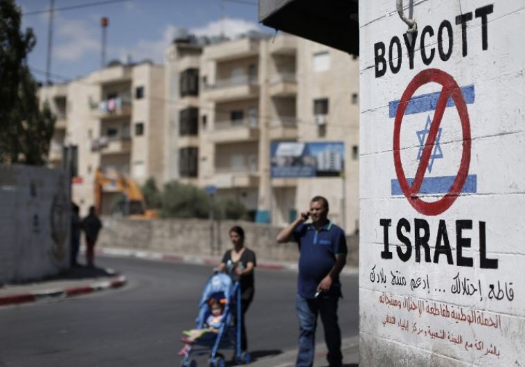 Palestinians walk past a sign calling for a boycott of Israel painted on a wall in Bethlehem