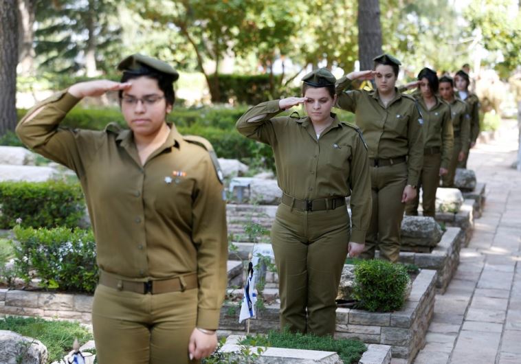 Israeli soldiers salute as they stand next to graves of fallen soldiers at Mt. Herzl cemetery