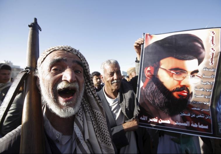 A Houthi militant shouts slogans as he stands next a poster of Hezbollah leader Hassan Nasrallah