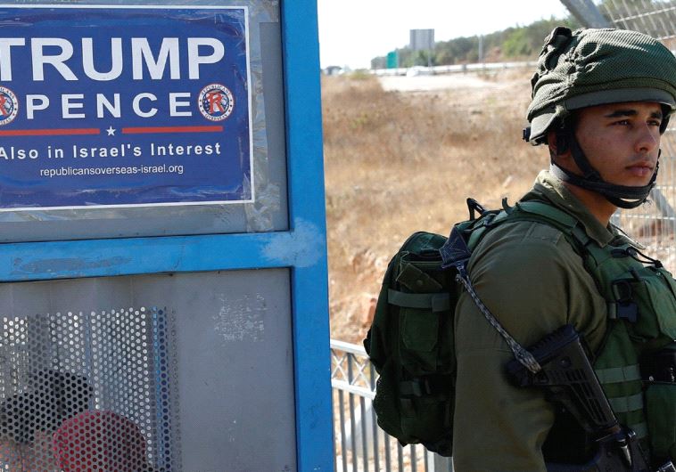 A soldier stands next to a bus stop with a pro-Trump poster near the West Bank Jewish settlement of 