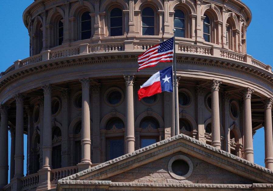 The US and Texas State flags fly over the Texas State Capitol in Austin