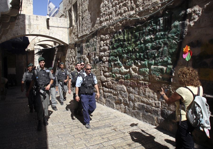 A tour guide (R) walks near Israeli police and border police officers in Jerusalem's Old City.