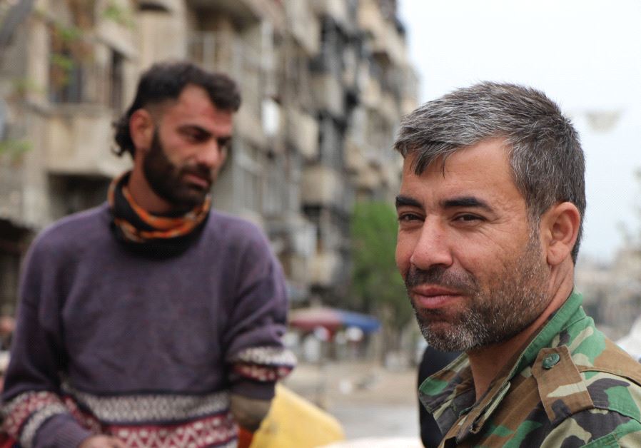 A volunteer with the Iranian-trained National Defense Forces is seen with a disabled veteran of the Syrian Army in the Bustan al-Qasr neighborhood of Aleppo (Jonathan Spyer)