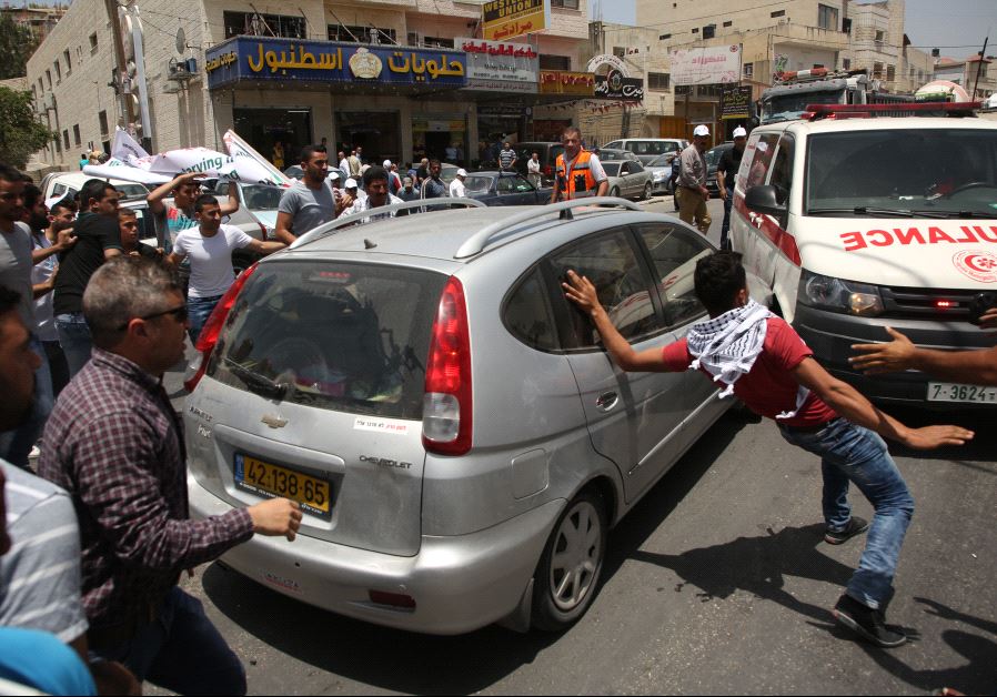 Palestinian protesters surround a car reportedly driven by an Israeli settler as it attempts to cross a crowd of demonstrators near the Hawara military checkpoint in the West Bank on May 18, 2017. (JAAFAR ASHTIYEH / AFP)