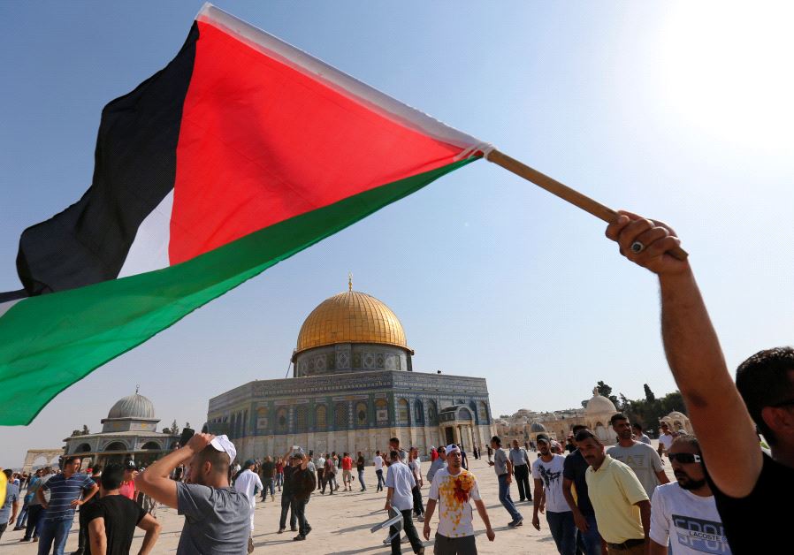 The Dome of the Rock is seen in the background as a man waves a Palestinian flag upon entering the T