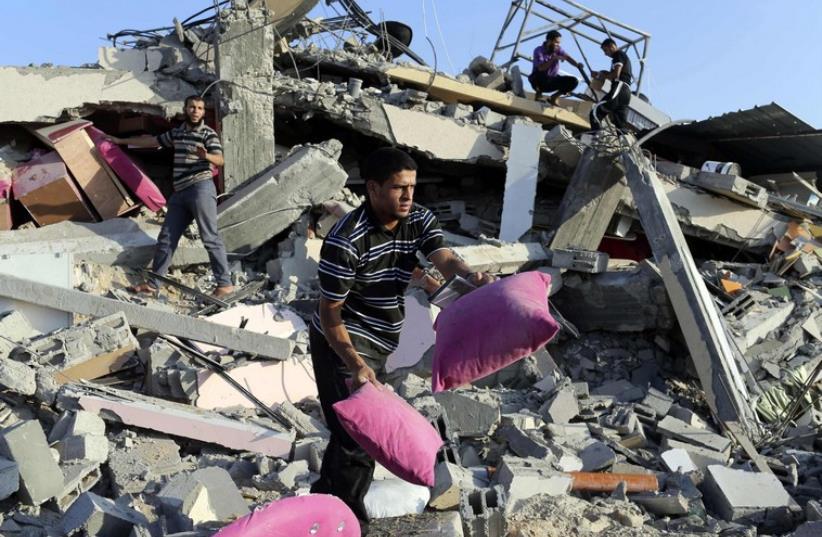 Palestinians collect their belongings from the rubble of their house which police said was destroyed in an Israeli air strike in Rafah in the southern Gaza Strip July 9, 2014 (photo credit: REUTERS)