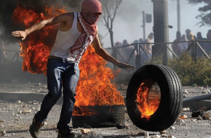 A stone-thrower stands next to a tire set ablaze during clashes with police in Shuafat. (photo credit: REUTERS)