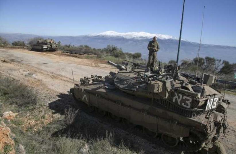 An IDF soldier stands atop a tank near the Lebanese border (photo credit: REUTERS)