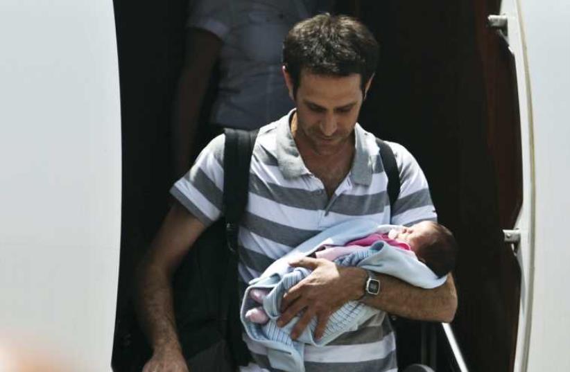 An Israeli man holds his baby, born to a surrogate mother, after being evacuated from Nepal and landing at Sde Dov Airport in Tel Aviv on April 27. (photo credit: NIR ELIAS / REUTERS)