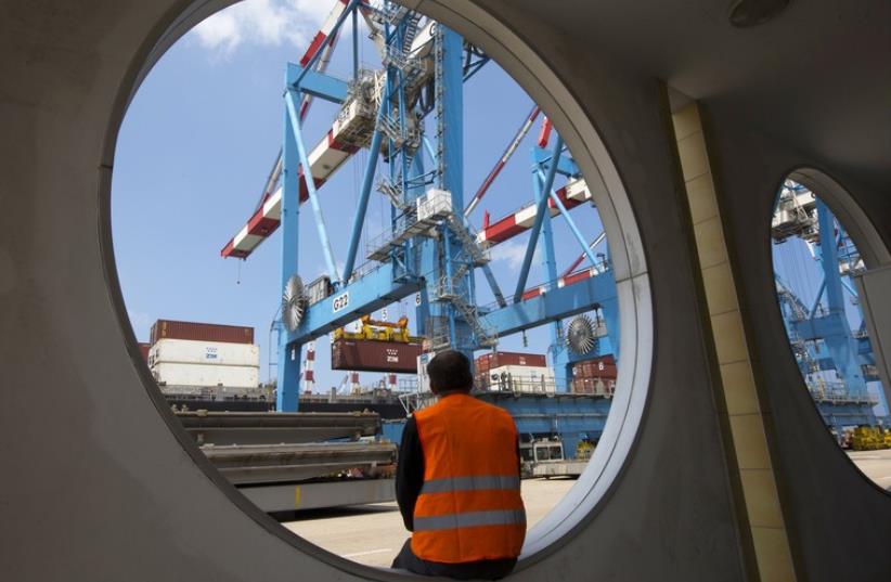 A worker sits as a crane unloads containers from a ship at the port of the northern city of Haifa (photo credit: REUTERS)
