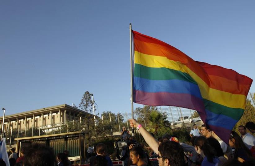 An activist waves an LGBT flag near Israel's Knesset building (photo credit: REUTERS)