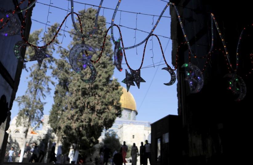 Palestinians walk next to decorations at the entrance to the compound of The Dome of the Rock ahead of the upcoming holy month of Ramadan in Jerusalem's Old City, June 11, 2015 (photo credit: REUTERS)