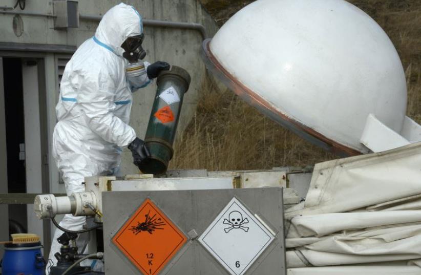 A worker dressed in protective clothing, handles a dummy chemical World War Two weapon. (photo credit: REUTERS)