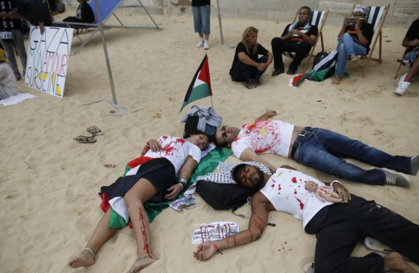 People covered in mock blood near a Palestinian flag and a placard which reads, "Gaza - My Love on Seine" stage their death on a artificial sand beach at "Paris Plages" to protest the "Tel Aviv on Seine" event, in Paris (photo credit: REUTERS)