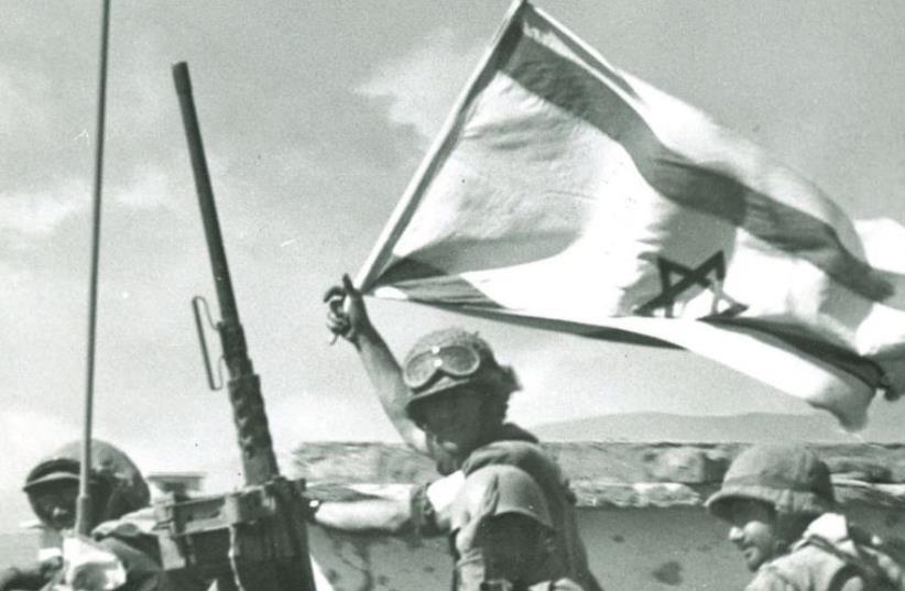 A soldier waves an Israeli flag on the Golan front during the Yom Kippur war. (photo credit: IDF SPOKESPERSON'S UNIT,JERUSALEM REPORT ARCHIVES)