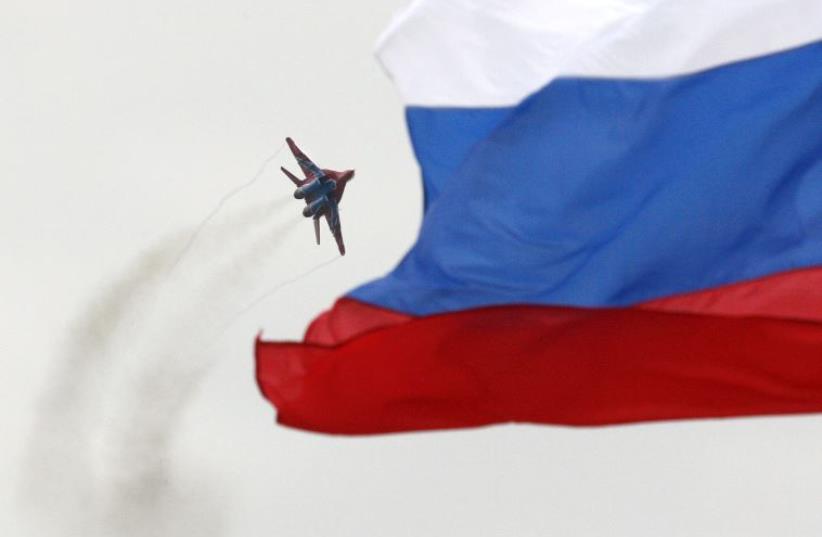 A MiG-29 fighter jet performs a manoeuvre as the Russian national flag flies in the foreground (photo credit: REUTERS)