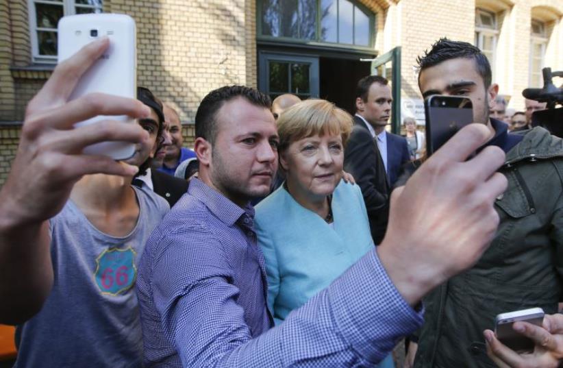 Migrants from Syria and Iraq take selfies with German Chancellor Angela Merkel outside a refugee camp near the Federal Office for Migration and Refugees after their registration at Berlin's Spandau district, Germany, September 10, 2015 (photo credit: REUTERS)