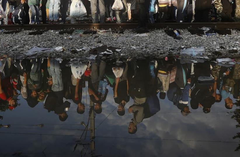 Syrian refugees are reflected in a puddle as they wait for their turn to enter Macedonia at Greece's border (photo credit: REUTERS)