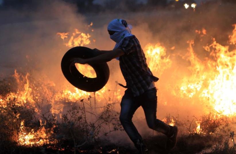 A Palestinian protester throws a tire into a fire during clashes with Israeli security forces (photo credit: AFP PHOTO)