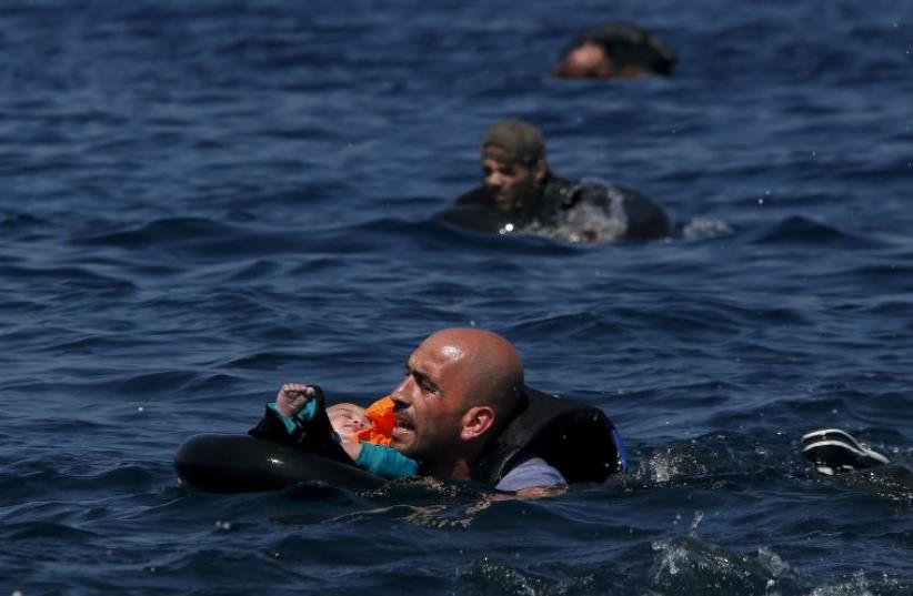 A Syrian refugee holding a baby in a lifetube swims towards the shore after their dinghy deflated some 100m away before reaching the Greek island of Lesbos (photo credit: REUTERS)