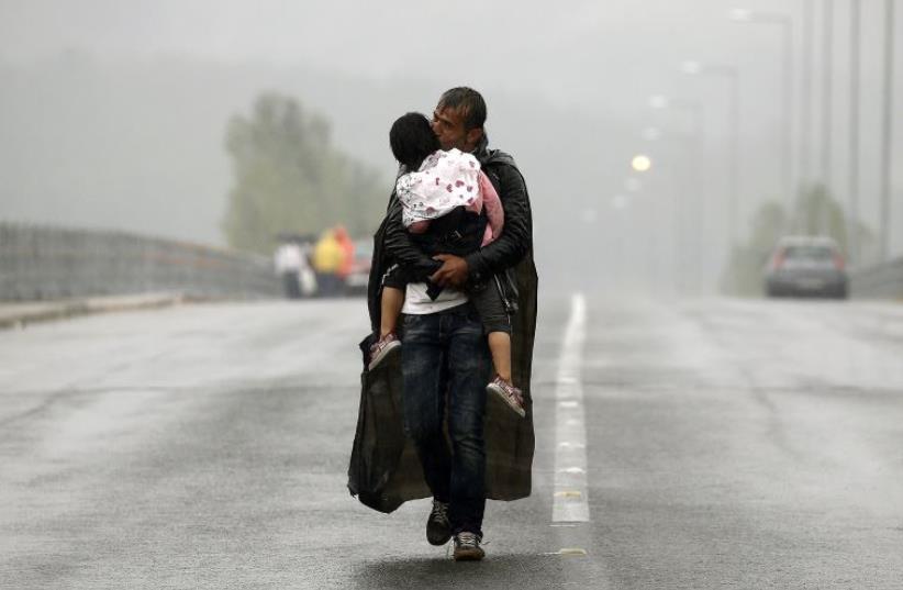 A Syrian refugee kisses his daughter as he walks through a rainstorm towards Greece's border with Macedonia, near the Greek village of Idomeni (photo credit: REUTERS)