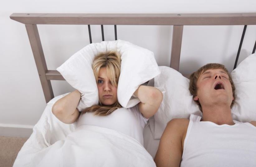 Illustrative: Frustrated woman covering ears with pillow while man snoring in bed (photo credit: INGIMAGE)