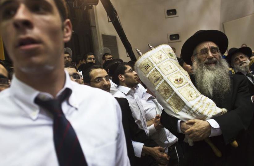 An Ultra-Orthodox Jewish Rabbi carries Torah scrolls as others dance during Simhat Torah celebrations in a synagogue in Bnei Brak (photo credit: REUTERS)