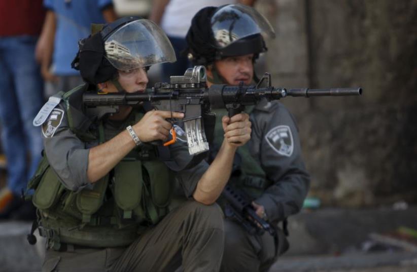 An Israeli border policeman aims his weapon at Palestinians during clashes in Hebron (photo credit: REUTERS)