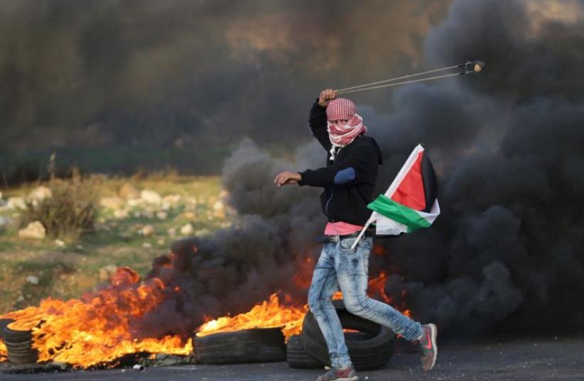 A Palestinian protester uses a sling to throw stones towards Israeli troops during clashes, near the Jewish settlement of Bet El, near the West Bank city of Ramallah November 29, 2015 (photo credit: REUTERS)