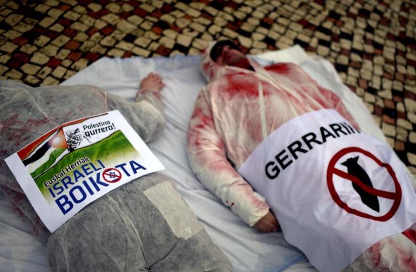 Demonstrators lie with posters in Basque which read, "Up With Palestinians. Boycott Israel" (L) and "No To War" as they wear suits covered in fake blood during a pro-Palestinian protest at the Plaza Moyua in Bilbao (photo credit: REUTERS)