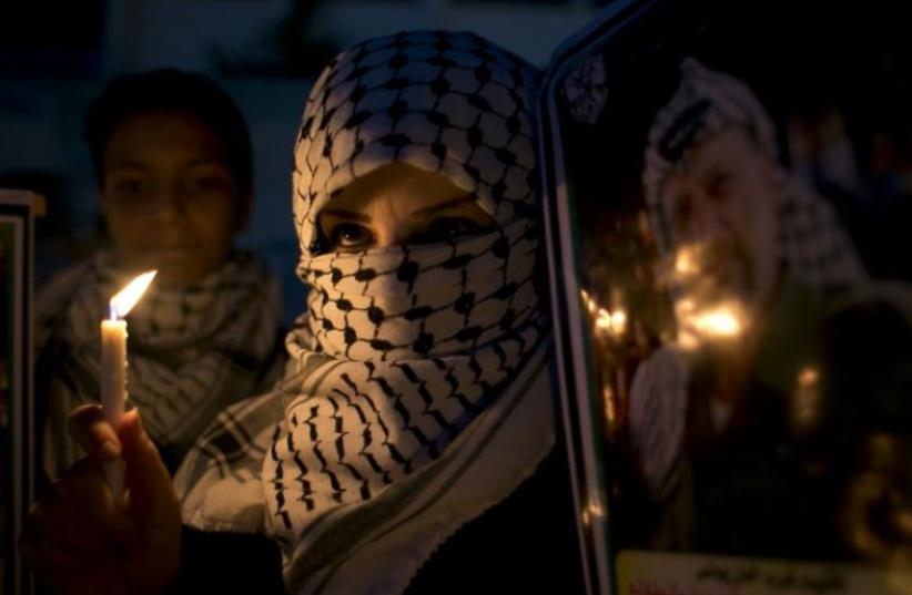 A Palestinian woman holds a candle during a protest in the southern Gaza Strip town of Khan Younis (photo credit: AFP PHOTO)