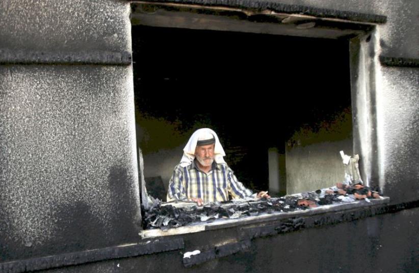 A man looks out of a house badly damaged by a firebomb attack by suspected Jewish extremists in the Palestinian village of Duma in the West Bank, July 31, 2015 (photo credit: REUTERS)