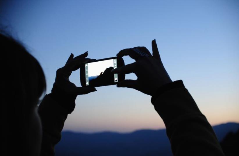 A girl takes photos on a smartphone (photo credit: REUTERS)