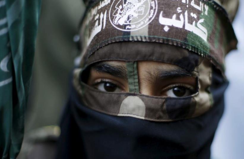 A masked Palestinian boy wearing the headband of Hamas's armed wing takes part in a rally marking the 28th anniversary of Hamas' founding in Gaza City (photo credit: REUTERS)