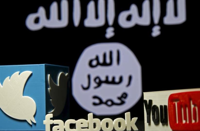 A 3D plastic representation of the Twitter and Youtube logo is seen in front of a displayed ISIS flag  (photo credit: REUTERS)