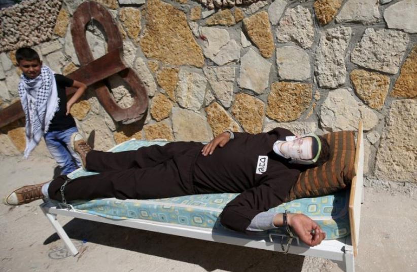 A Palestinian lies on a bed as he covers his face with a picture of Palestinian journalist Mohammad al-Qiq, who was detained by Israeli forces in November and is on an almost-three-month hunger strike (photo credit: REUTERS)