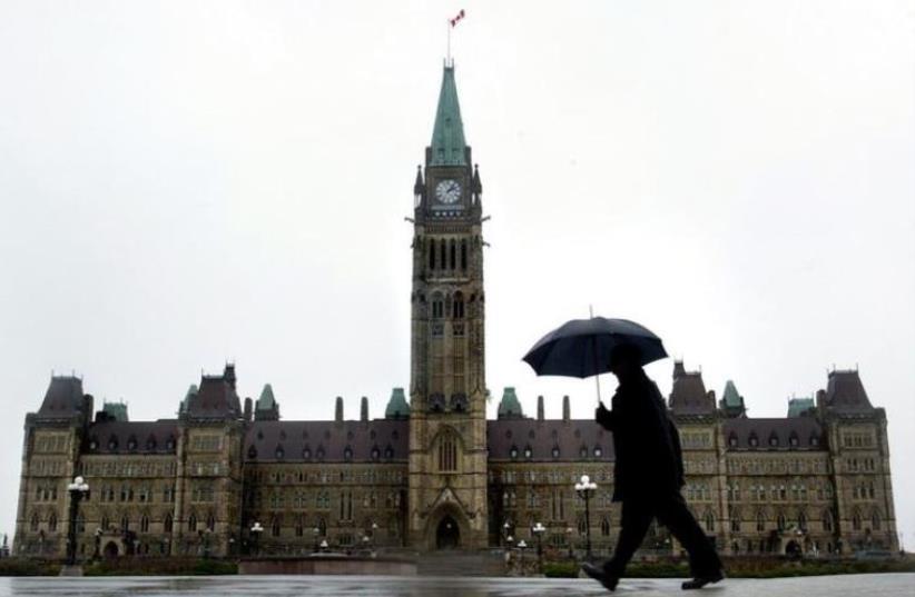 A pedestrian walks in the rain on Parliament Hill in Ottawa, Canada. (photo credit: REUTERS)