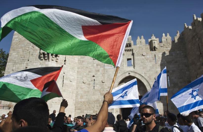 Palestinian protesters wave Palestinian flags as Israelis carrying Israeli flags walk past in front of the Damascus Gate outside Jerusalem's Old City (photo credit: REUTERS)