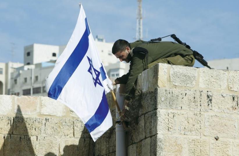 An Israeli solider removes the flag from a rooftop in Hebron as troops force Jewish settlers out of homes they said they had purchased from Palestinians (photo credit: REUTERS)
