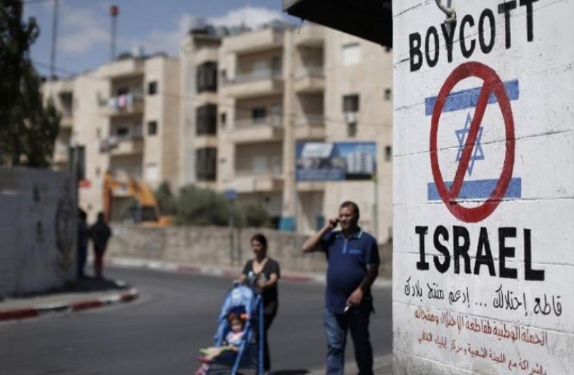 Palestinians walk past a sign calling for a boycott of Israel painted on a wall in Bethlehem (photo credit: AFP PHOTO)
