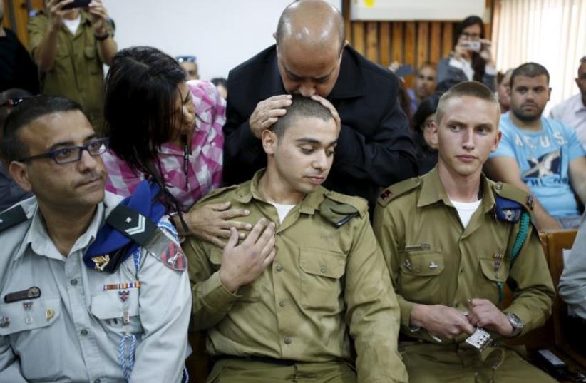 The father of Israeli soldier Elor Azaria, who is charged with manslaughter after he shot a wounded Palestinian assailant as he lay on the ground in Hebron on March 24, kisses his head in a military court (photo credit: REUTERS)